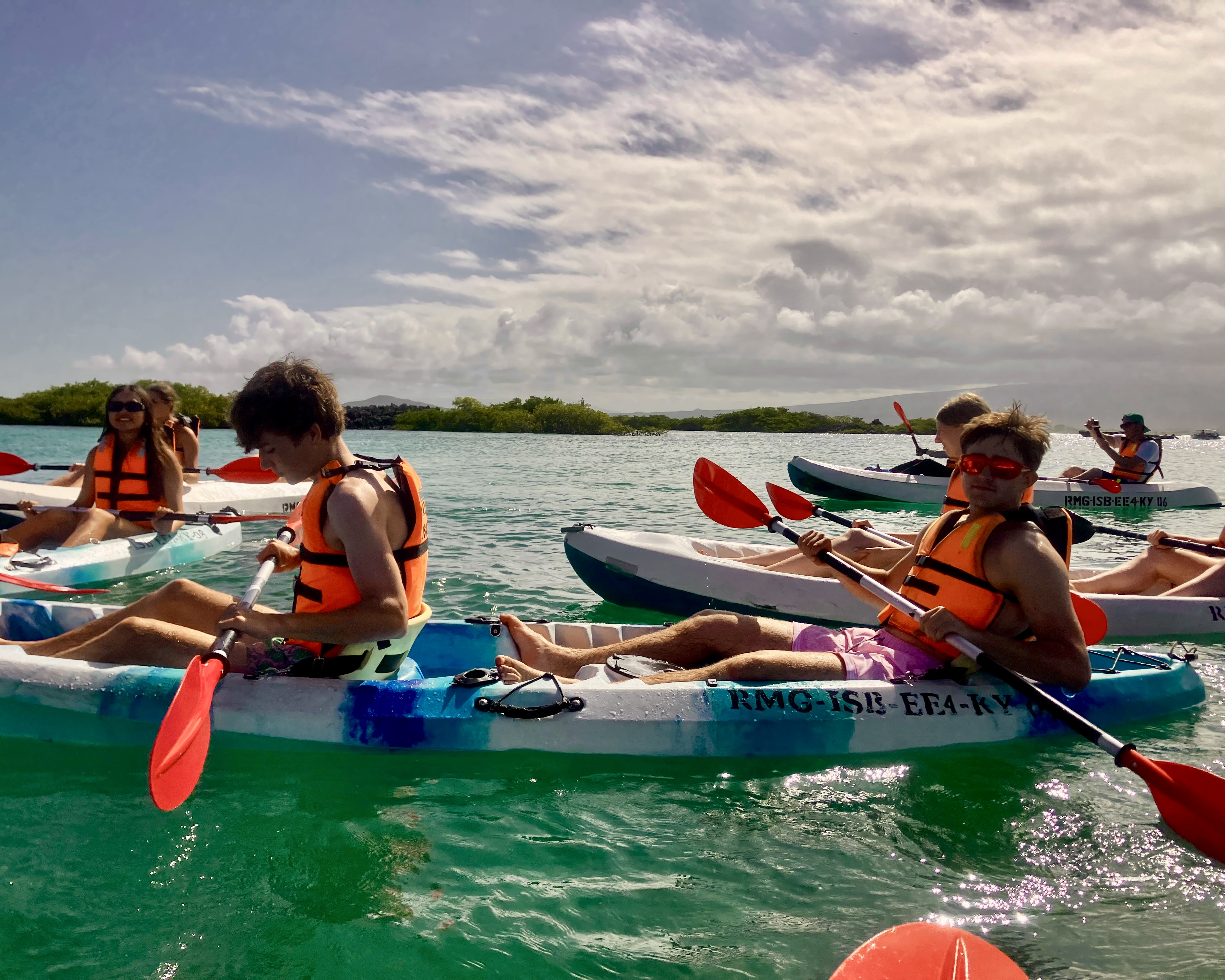 High school students in life jackets kayak through calm island waters in the Galapagos on an adventure summer program