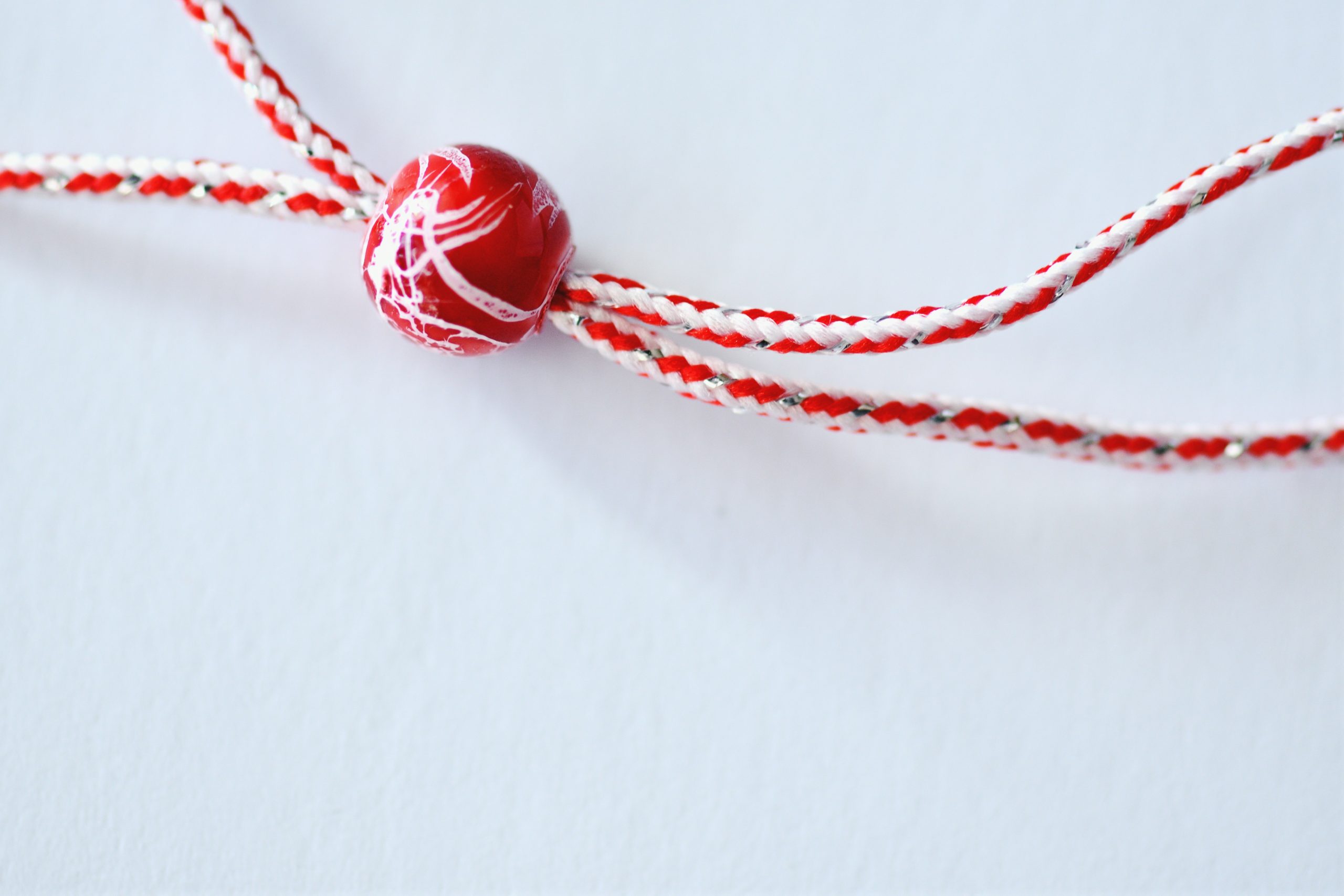A red and white martenitsa thread with a painted red bead, the token exchanged on the first of March.