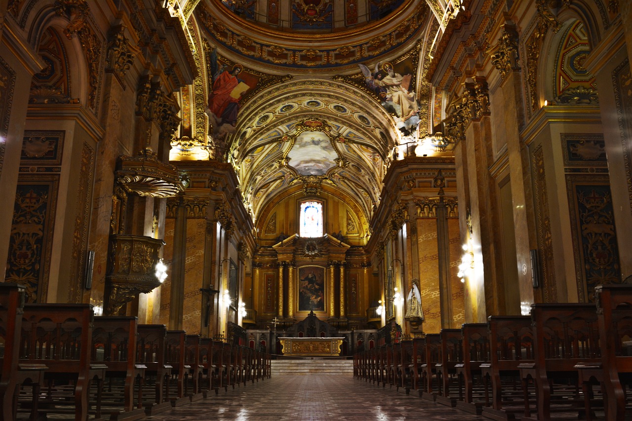 Ornate gilded cathedral interior with a domed ceiling and rows of wooden pews leading to the altar