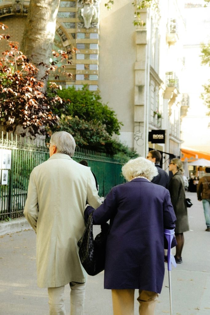 An elderly couple strolls down the street, arm in arm.