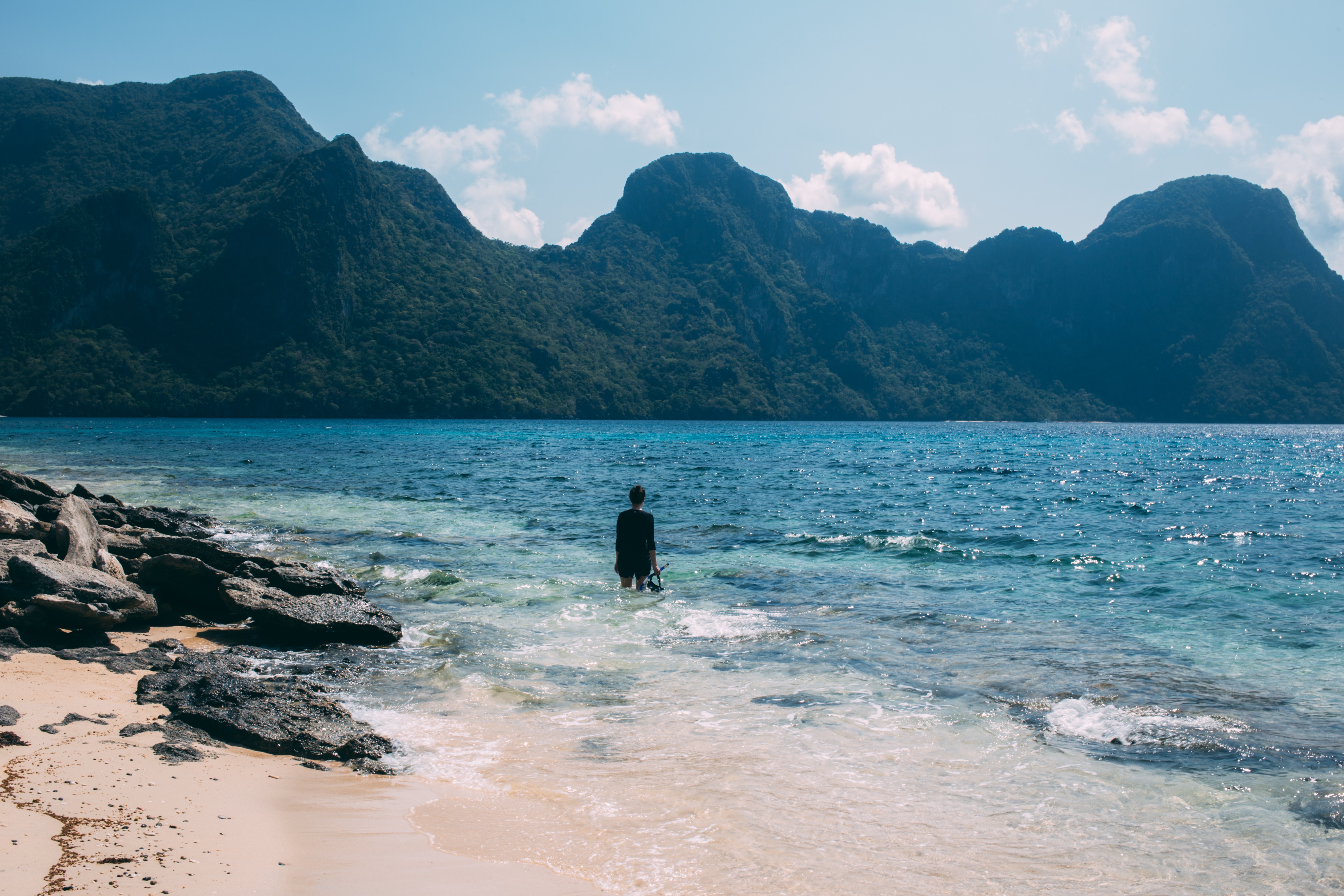 A student wades into calm water beneath dramatic mountain peaks