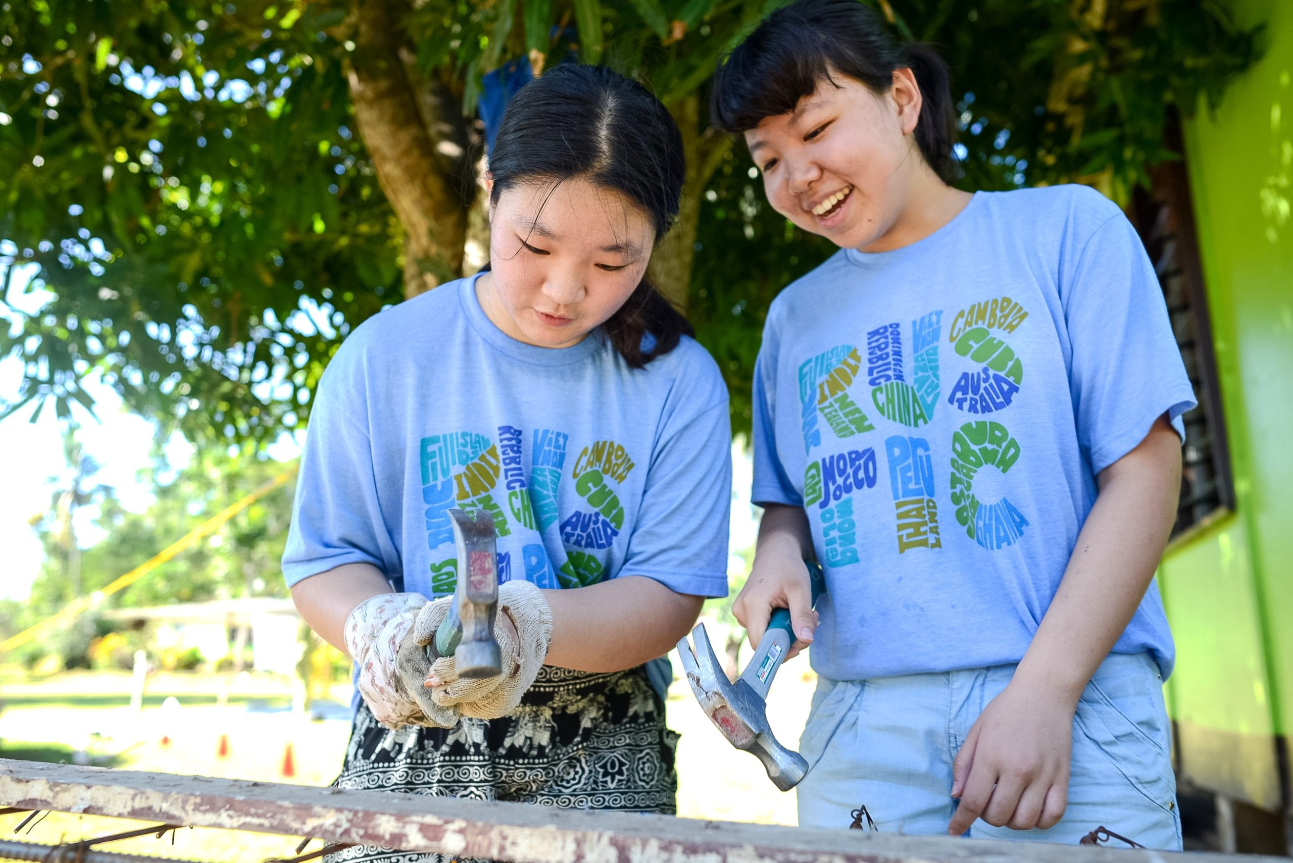 Two teens in blue shirts use hammers during a service project in Fiji, showcasing the impact of choosing teen travel for hands-on learning.