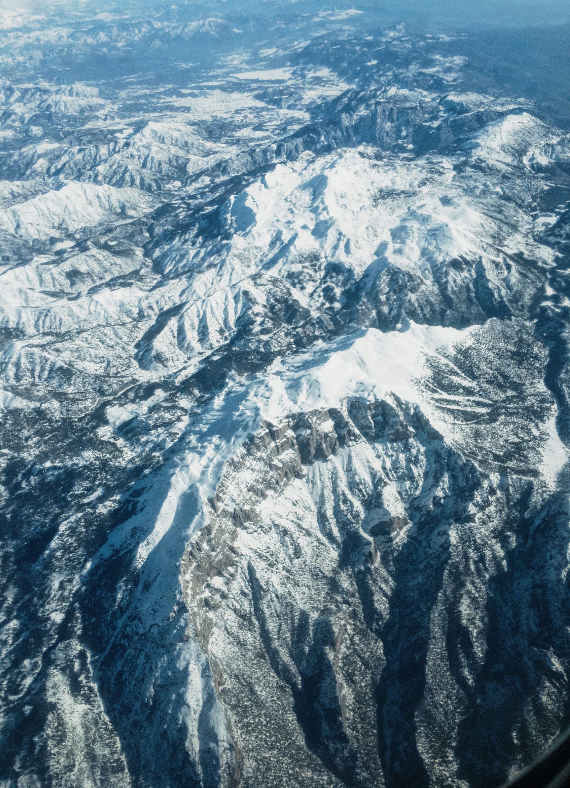 Aerial view of a snow-covered mountain range with rugged terrain and peaks extending into the distance.