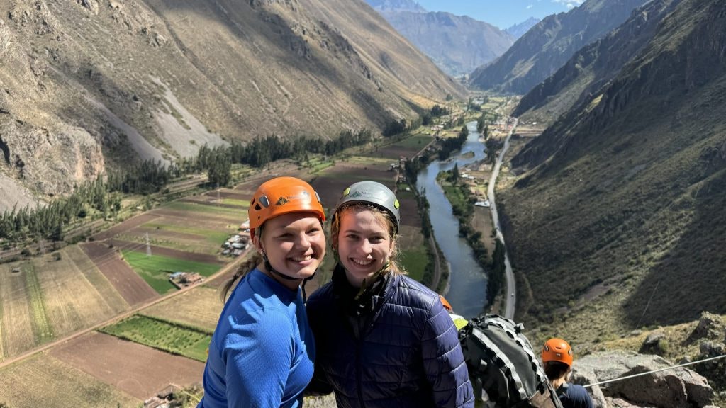 Two students in hardhats pose at a valley viewpoint during an outdoor program in Peru.