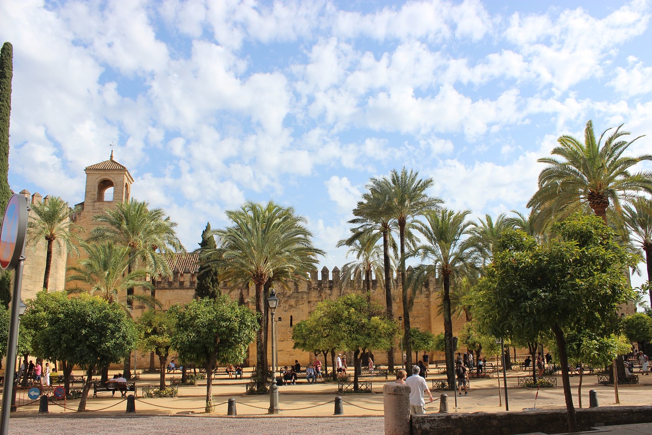 Palm-lined plaza beside a historic stone city wall under a partly cloudy sky