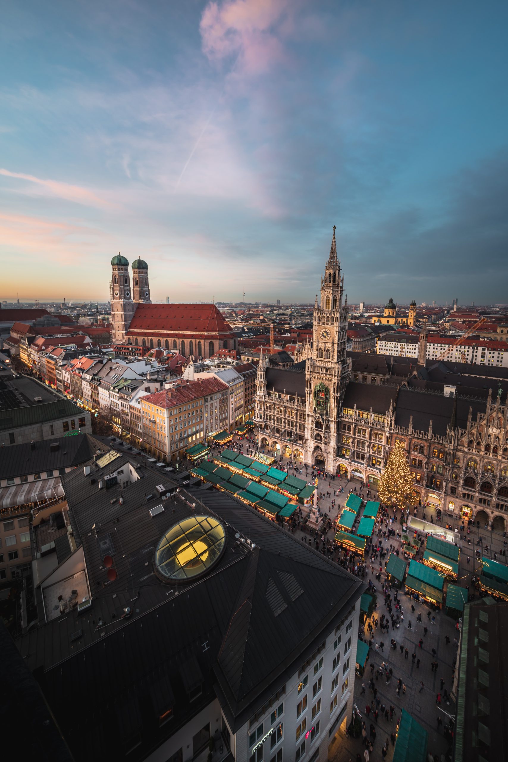 Teen travelers look out over Munich's Marienplatz, with market stalls and the New Town Hall tower glowing at dusk