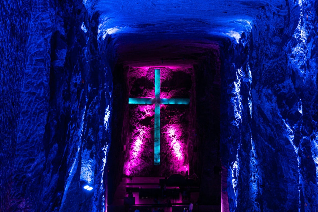 Inside Catedral de Sal, with the cross lighting up in blue, with a pink hue in the back. The walls are glowing in a dark blue color. 