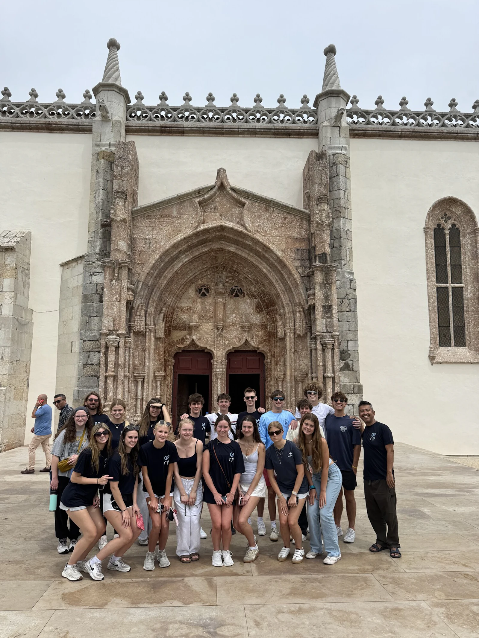 A group of teen travelers gathers in front of a carved stone church doorway in Lisbon, Portugal