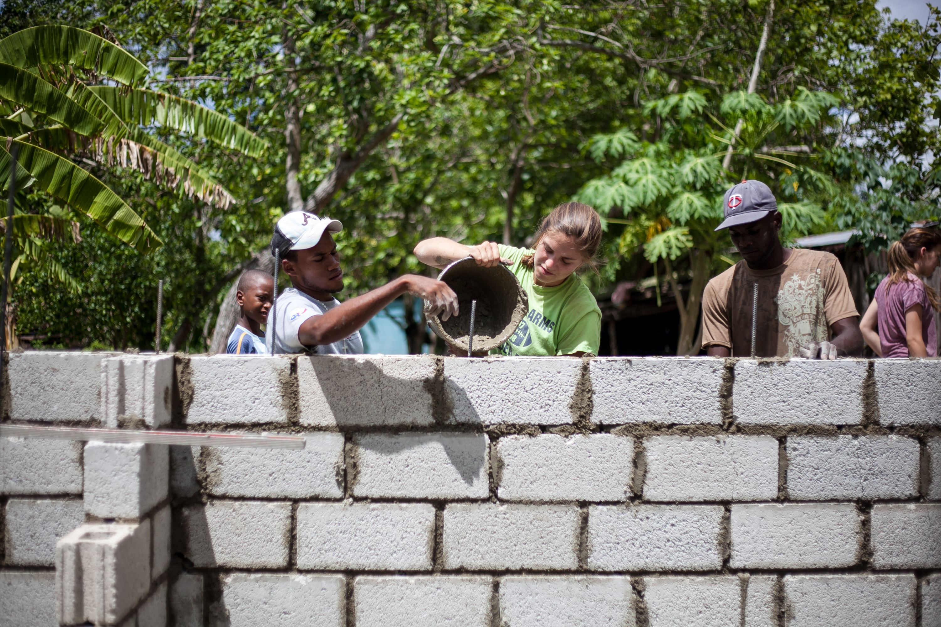 Students and community members pour concrete over a cinder block wall on a construction site