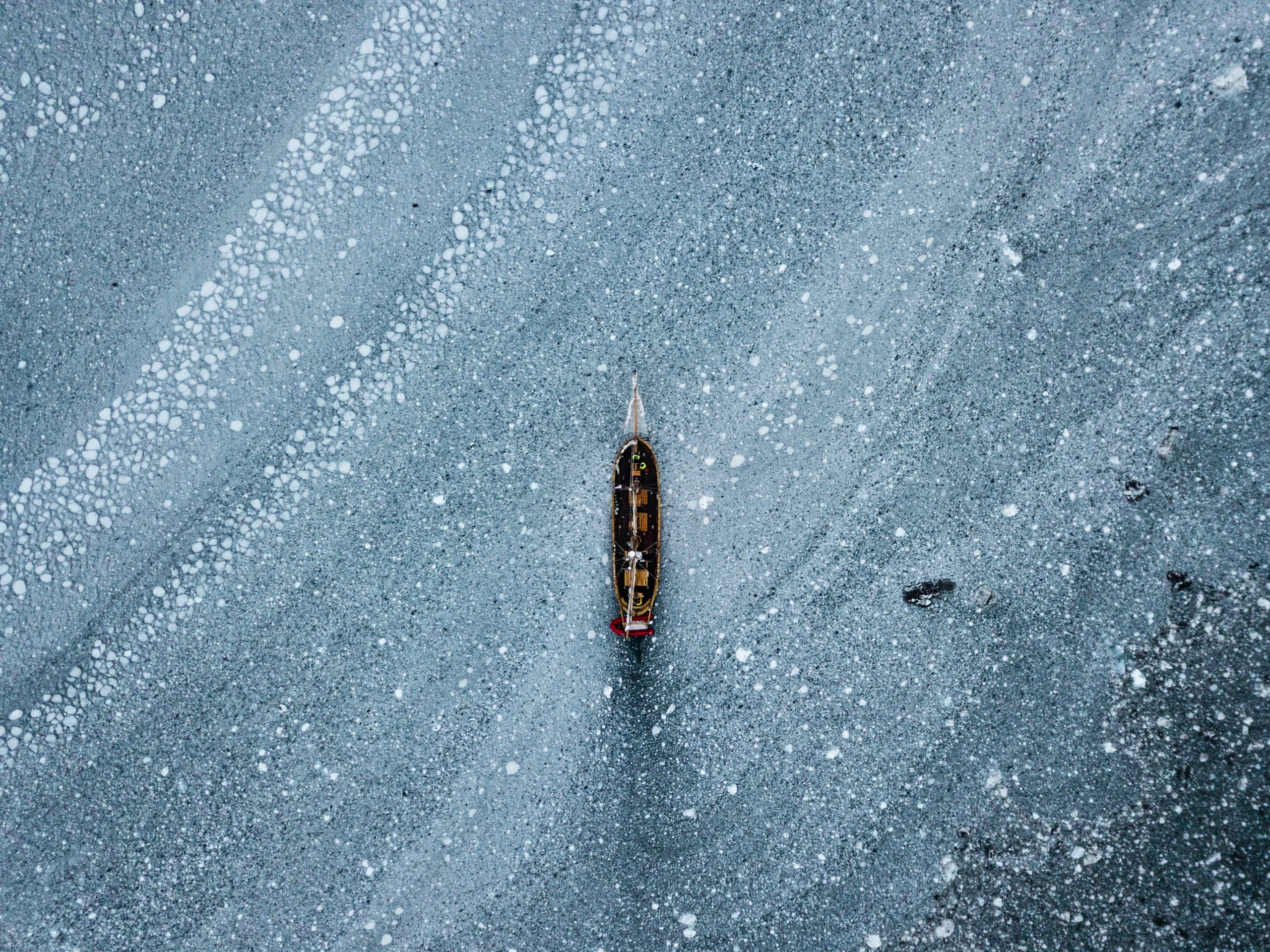 A lone wooden boat on a frozen body of water with a pattern of white spots on the icy surface.