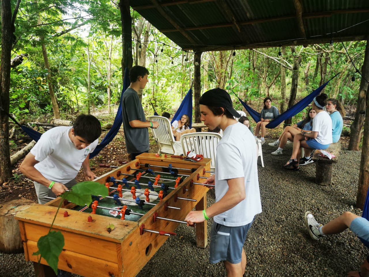 Picture of students gathered playing foosball with other students talking in the background.