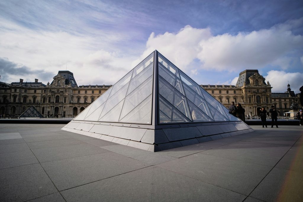 The glass pyramid of the Louvre Museum in Paris with a historic building in the background