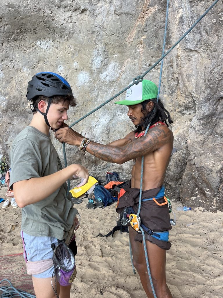 a rock climbing instructor helping a student with his equipment during an outdoor climbing activity.