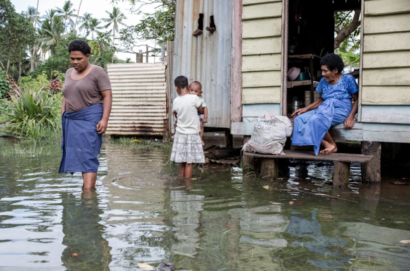 Fijian villagers wade through floodwaters near their home, highlighting the impact of rising sea levels on coastal communities.