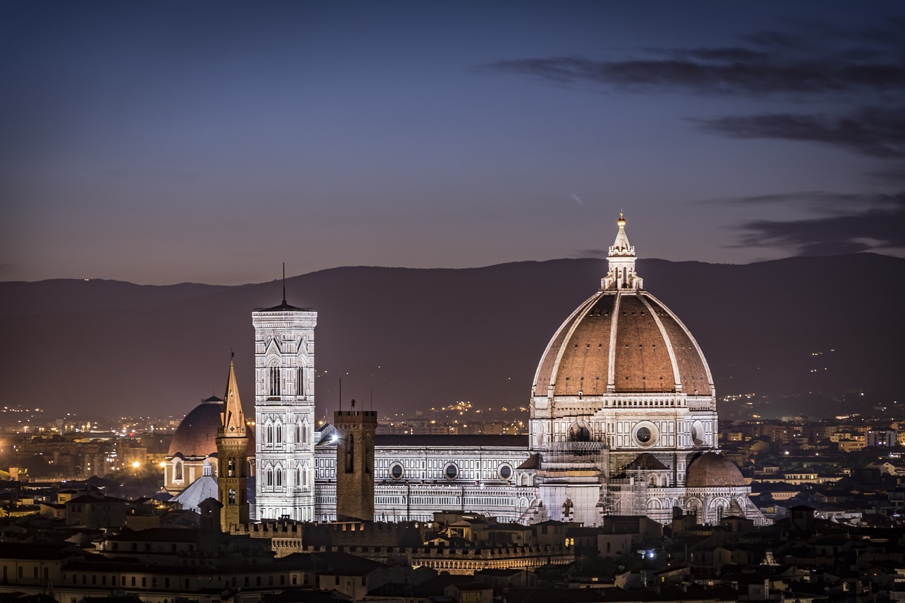 Florence Cathedral's dome and bell tower illuminated at dusk above the city skyline