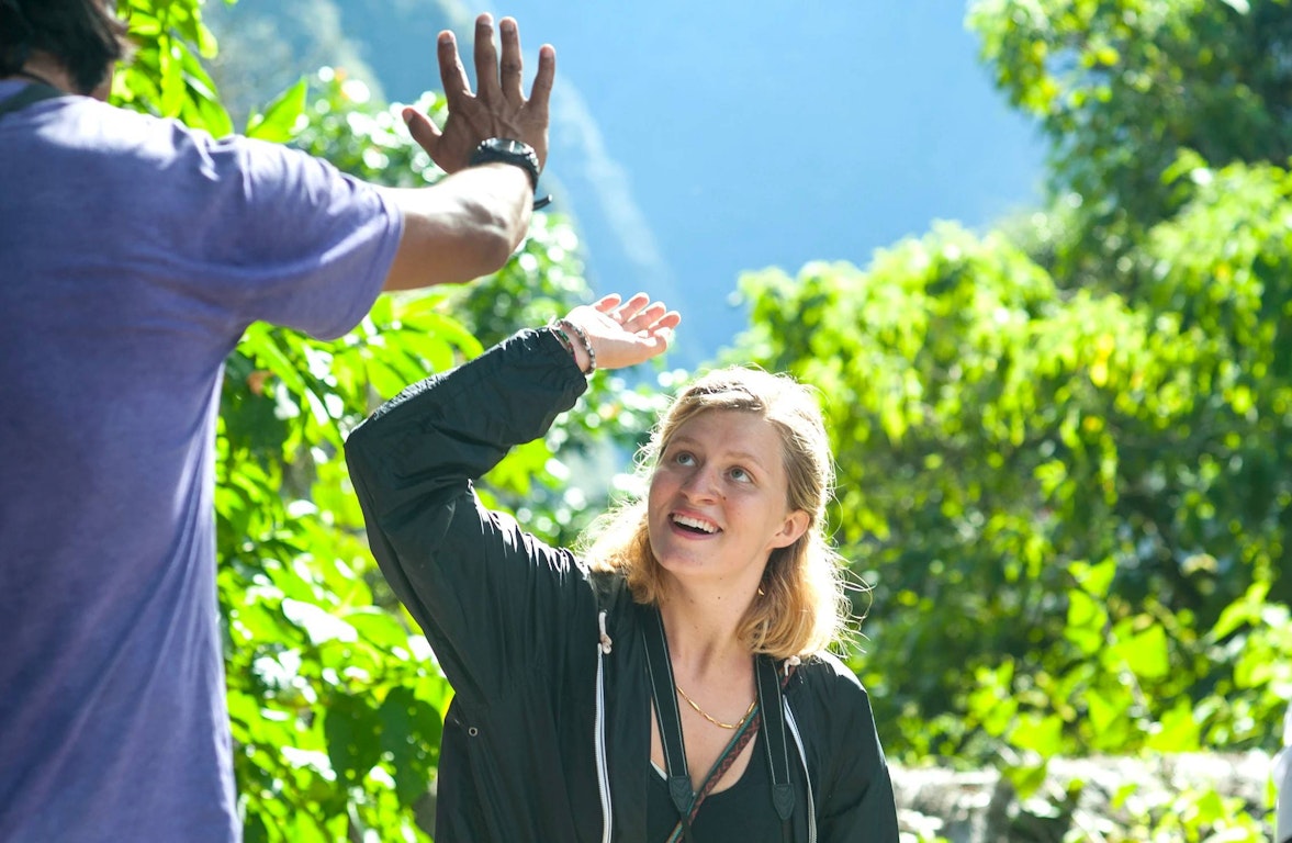 Young woman giving a high five on a gap year farm experience surrounded by lush greenery
