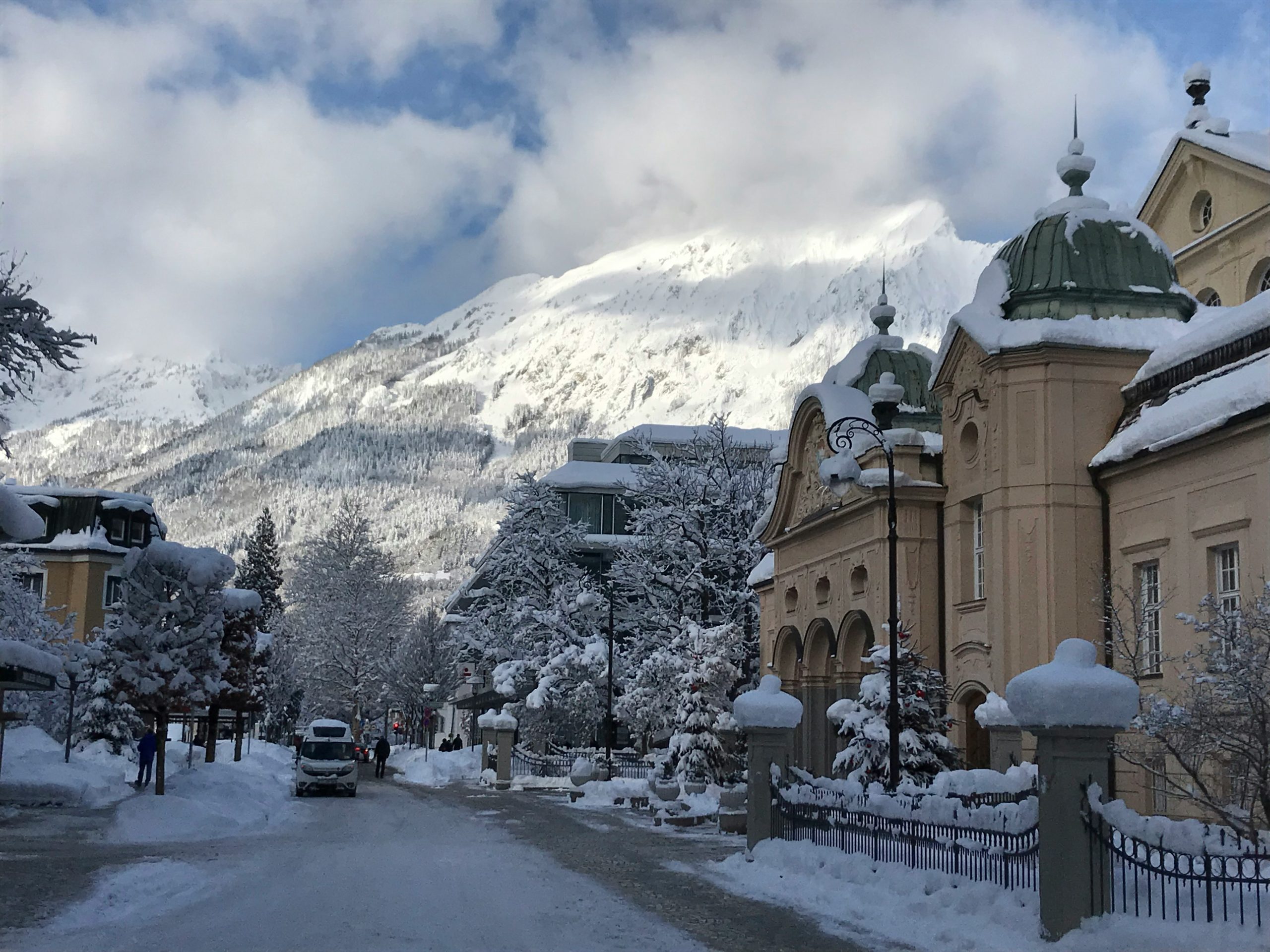 Snow-covered street lined with historic buildings beneath a cloud-wrapped alpine peak