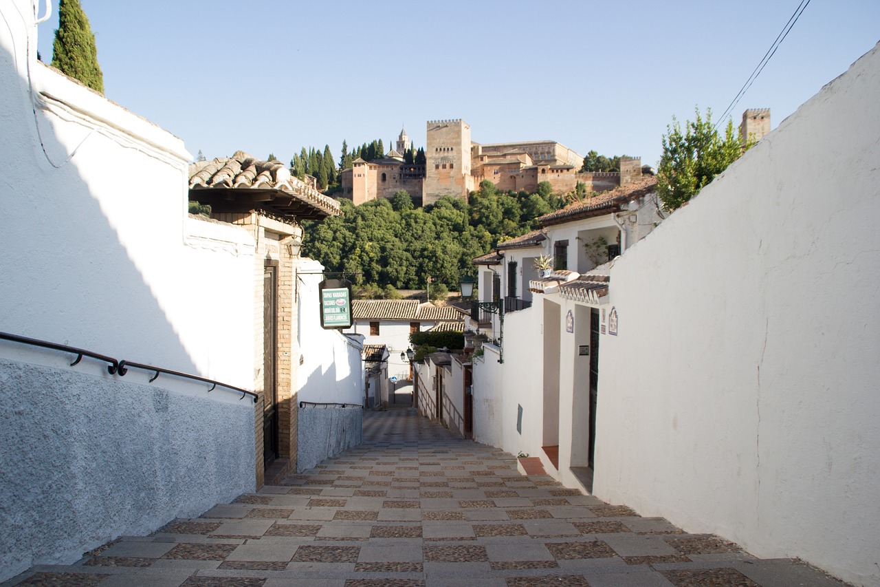 A narrow whitewashed alley in Granada's Albaicín leads toward the Alhambra on the hill above