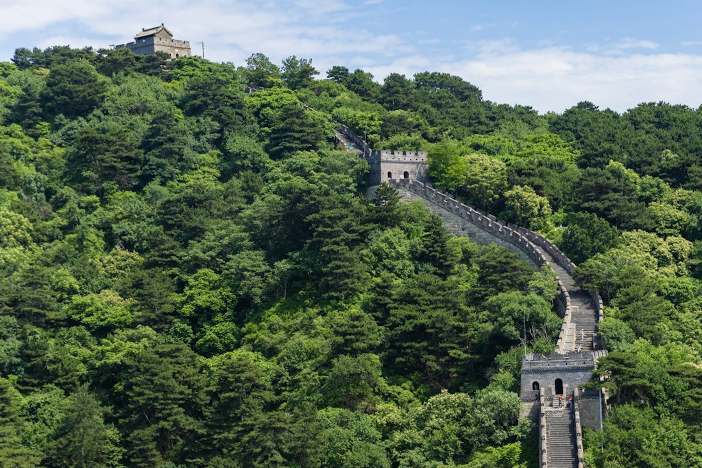 A restored section of the Great Wall of China climbing a forested ridge between stone watchtowers.