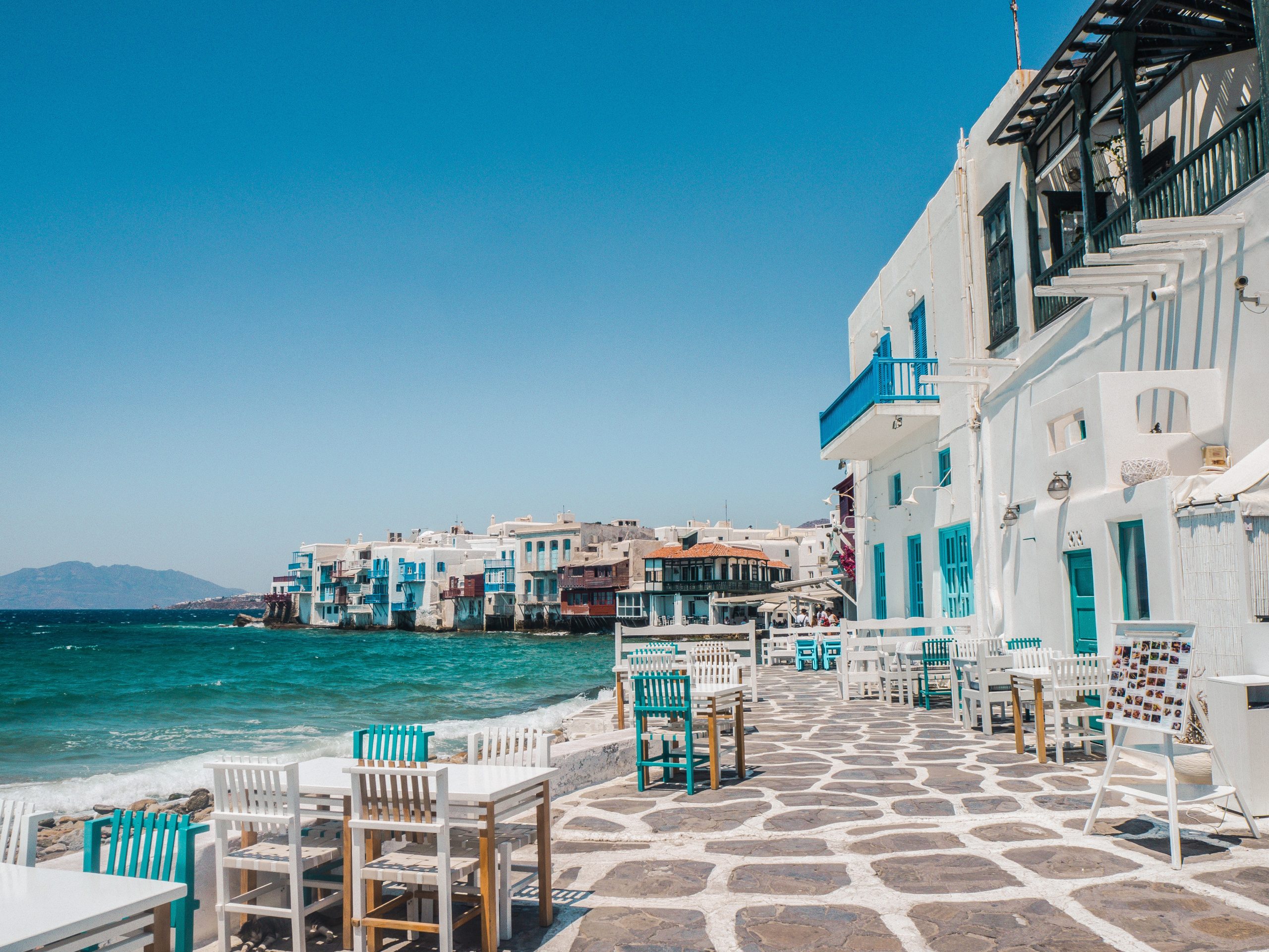 Street in Greece next to a body of water and many houses in the background.