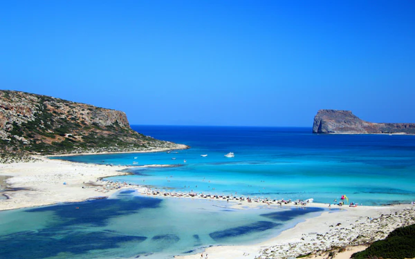 A turquoise lagoon behind a pale sandbar, with a rocky headland on one side and a flat-topped island offshore.