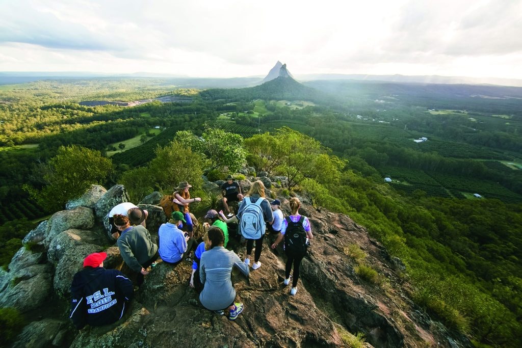A group of hikers sitting at the top of a hill looking out over a green valley below.