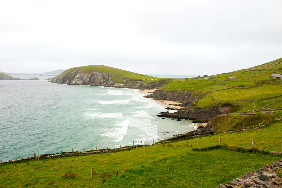 Green fields edged with stone walls run down to a curving sandy bay on the coast of Ireland