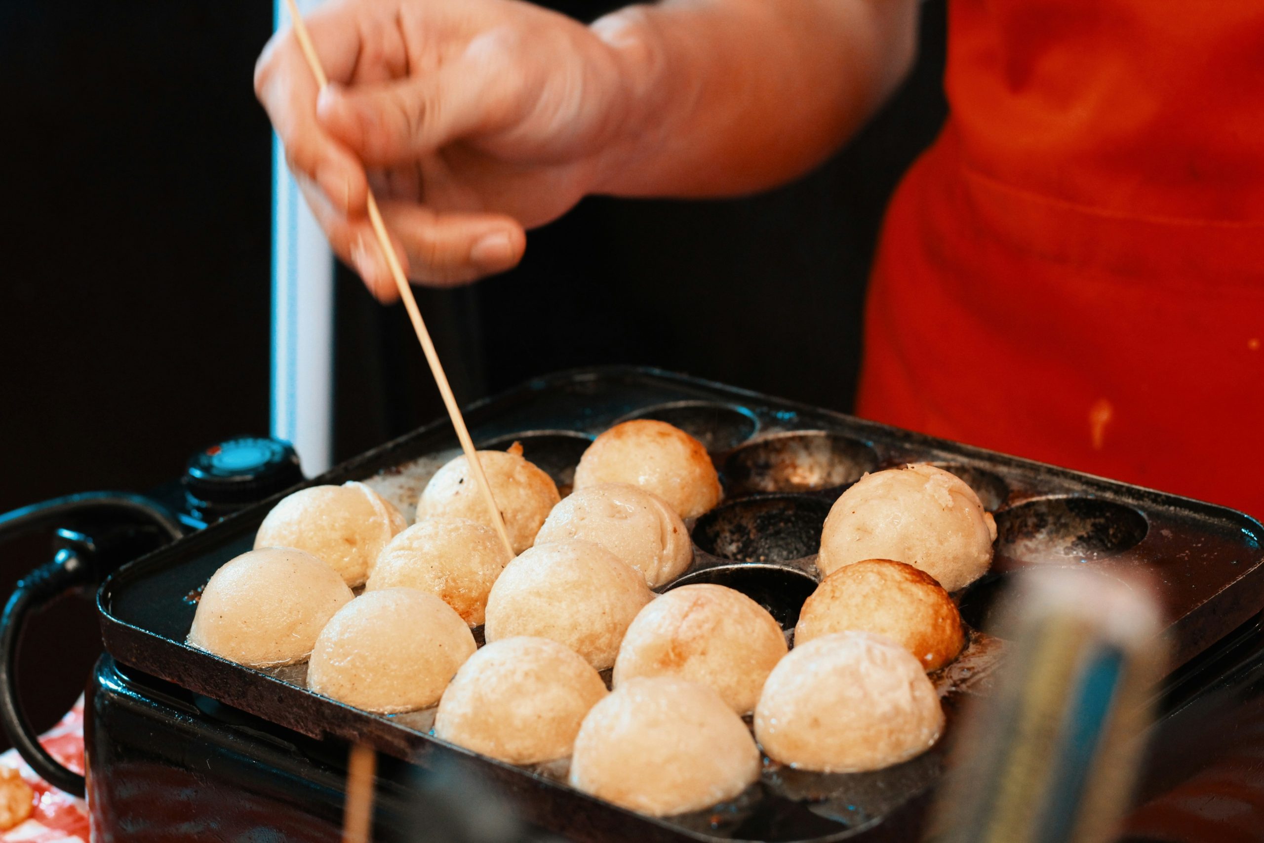 A close-up shot of someone cooking takoyaki.