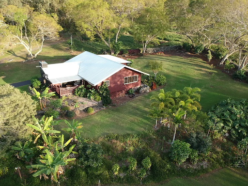 Aerial picture of house in Hawaii with trees and a lot of grass around it.