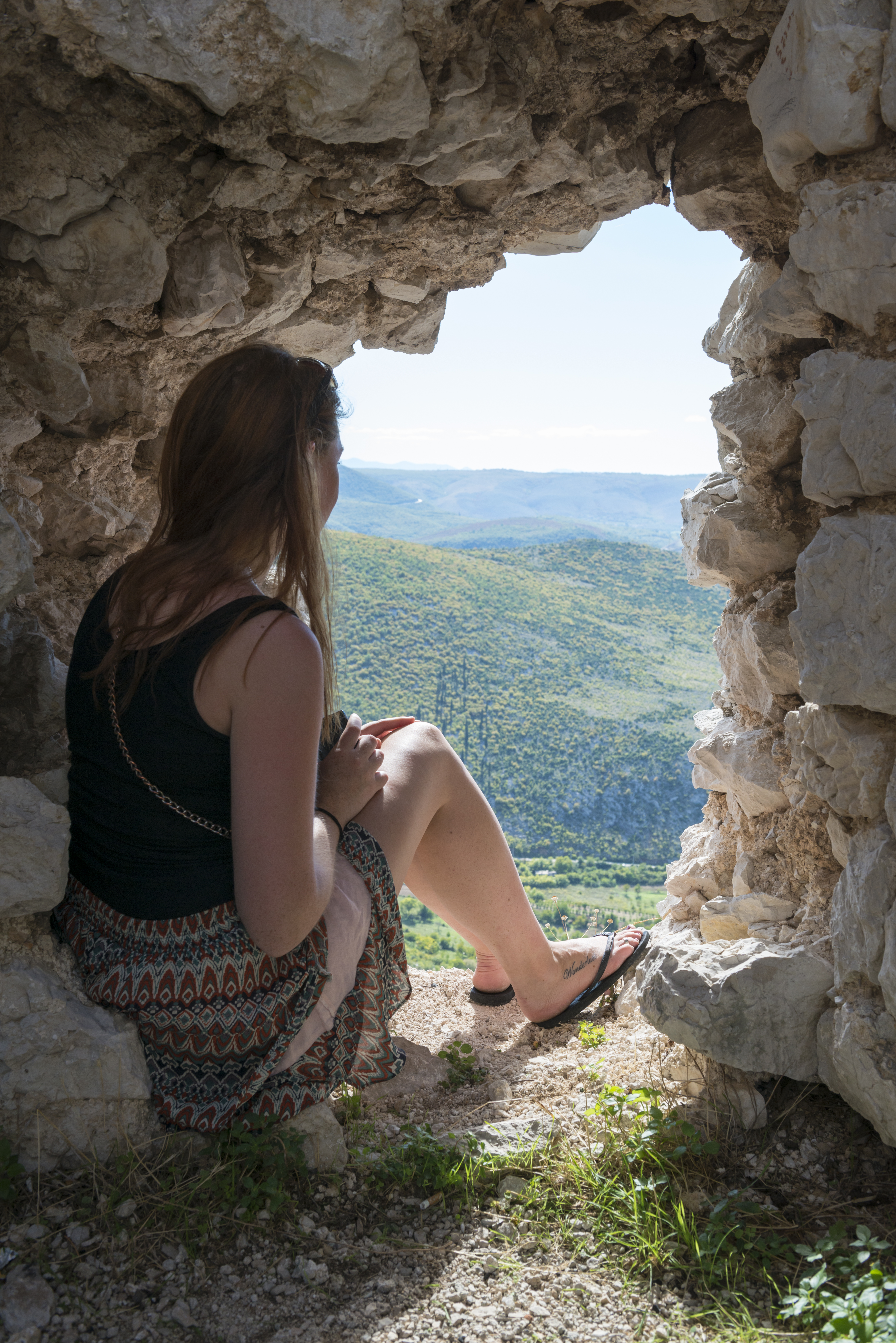 A student sits in a stone fortress window overlooking green hills