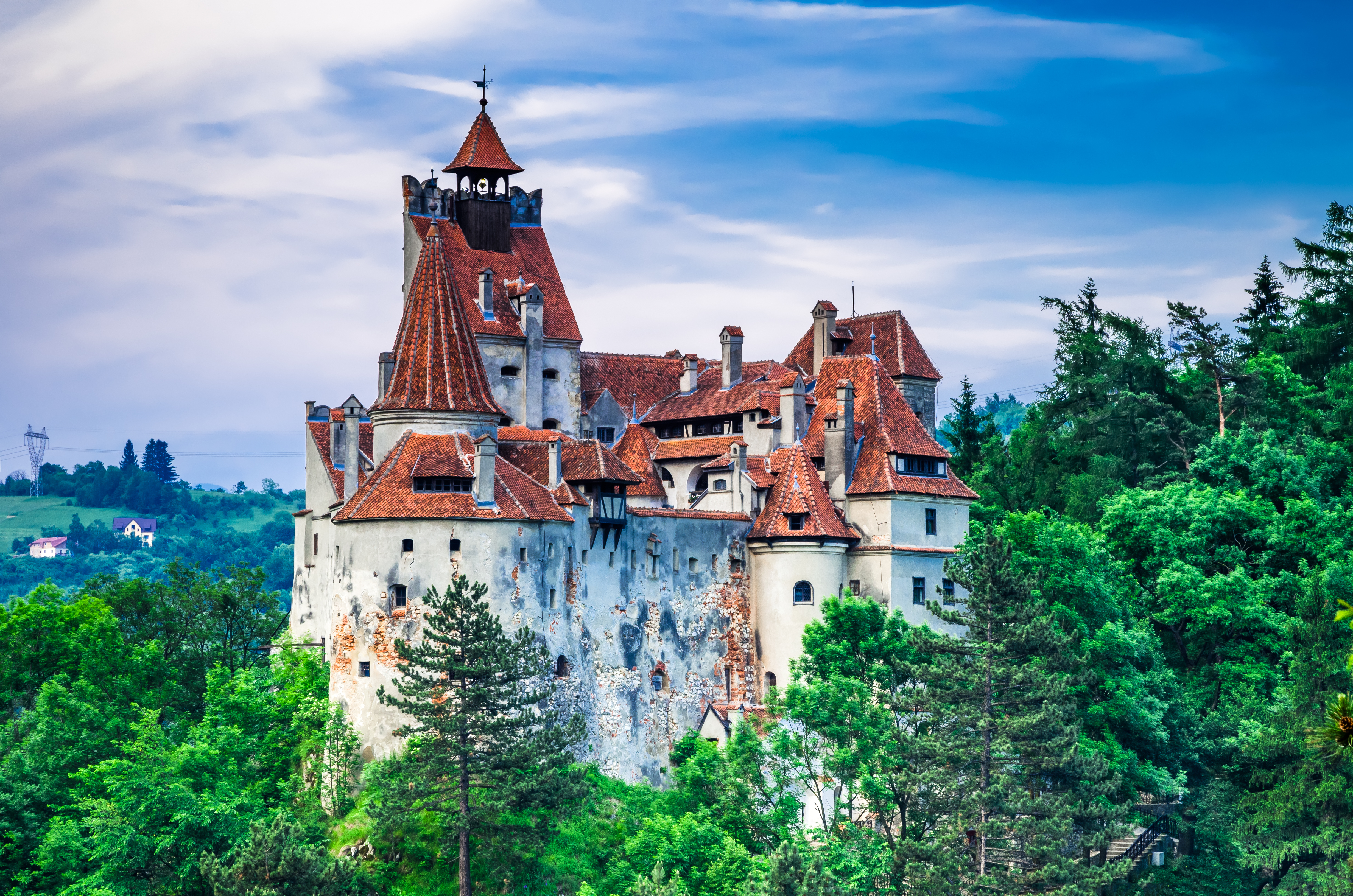Students pause below a medieval castle with red-tiled turrets rising above a hillside forest