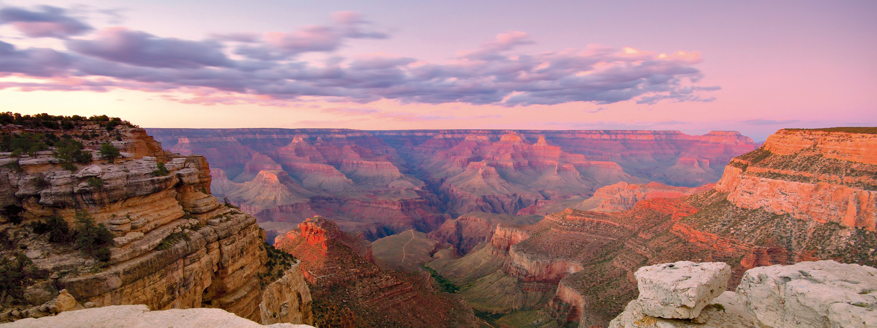 Layered canyon ridges glow pink and orange under a cloudy sunset sky at the Grand Canyon in the United States