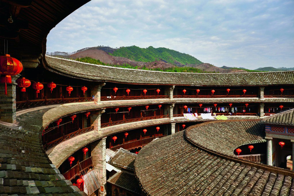 Traditional round Chinese tulou building with red lanterns and mountain backdrop. Fun facts about China