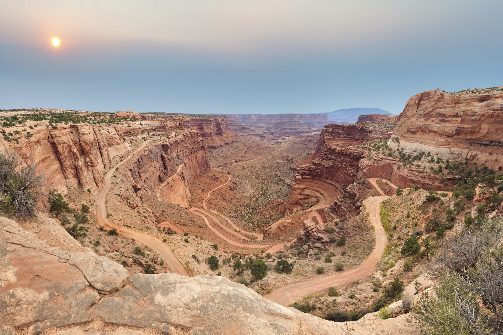 A switchback dirt road winds down into a red rock canyon at sunrise