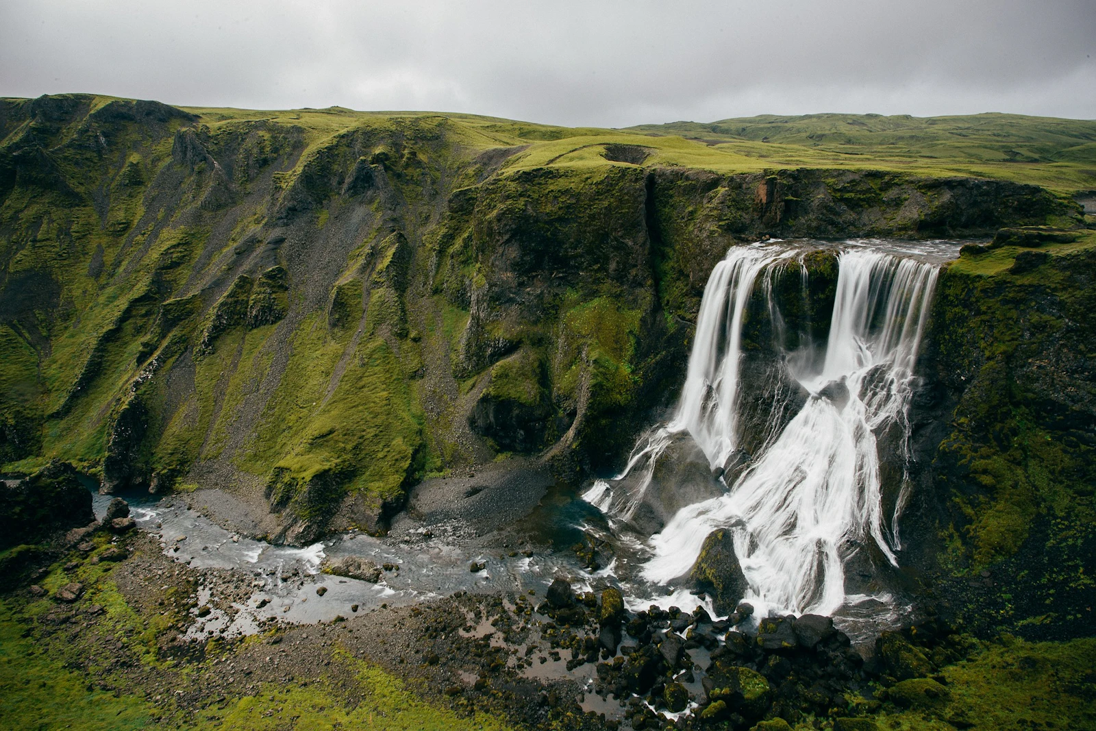 Twin waterfalls spill over a mossy green cliff into a rocky gorge