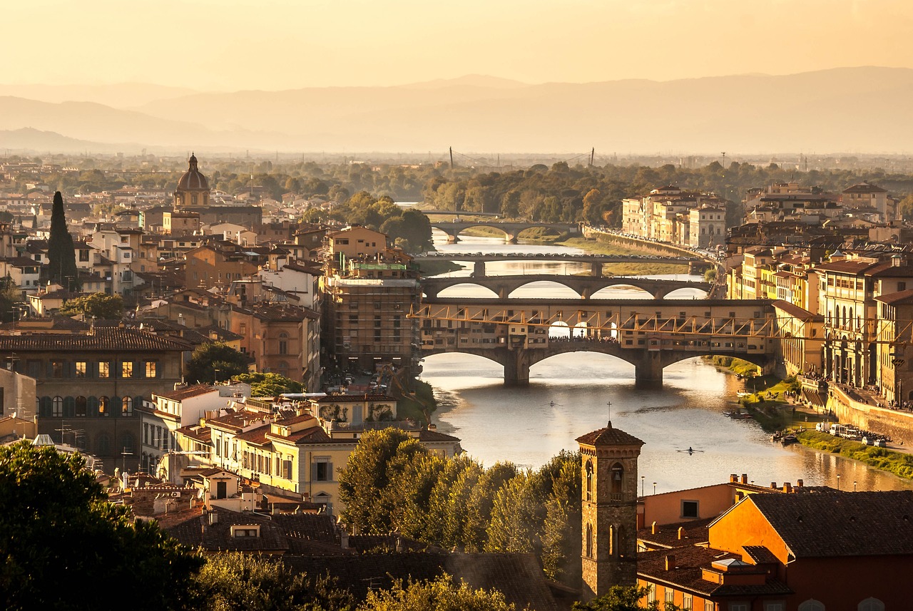 A school trip pauses where Ponte Vecchio spans the Arno River amid Florence's rooftops at golden hour