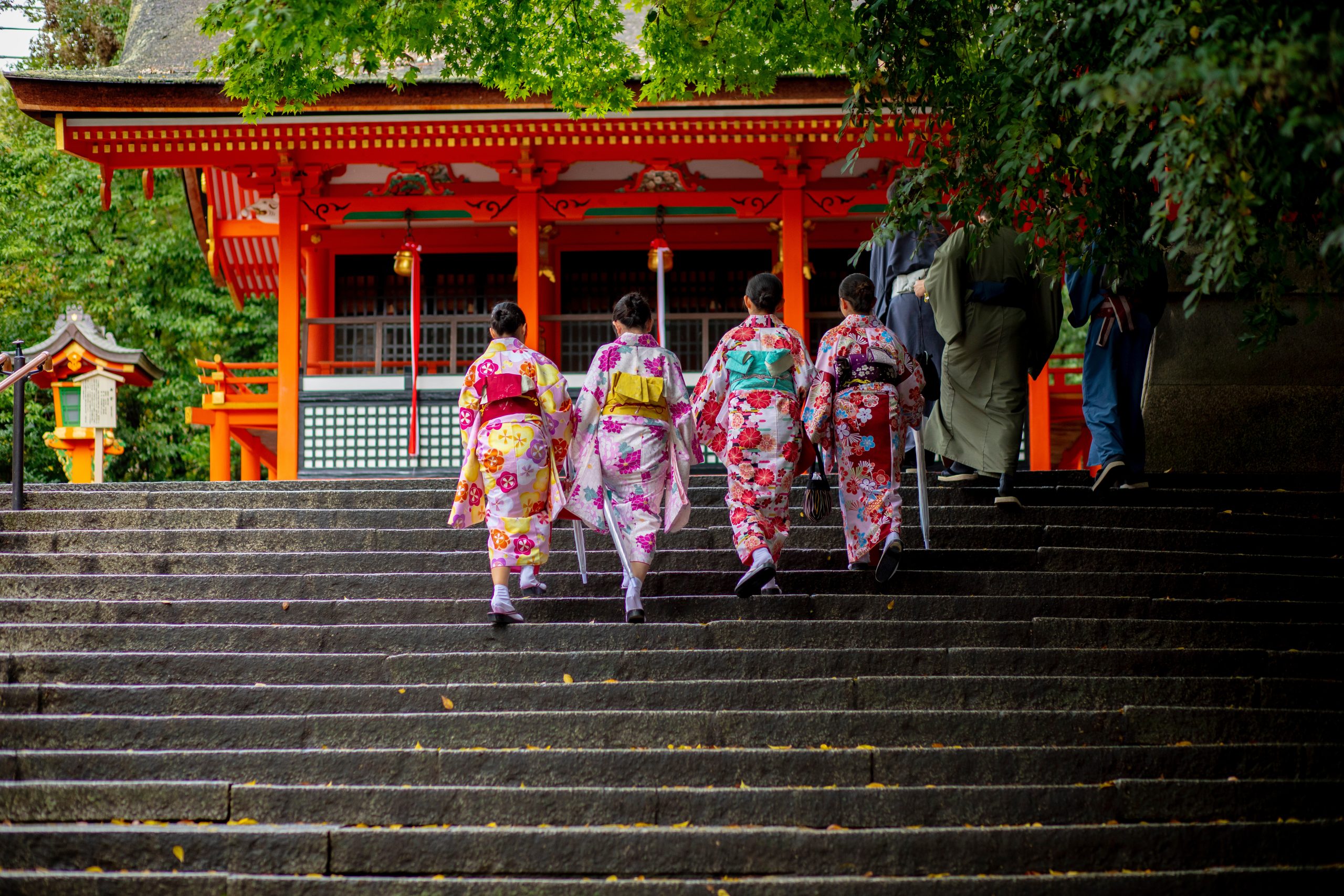 Students in colorful kimonos climb stone steps toward a red shrine gate