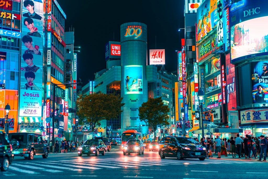 Night time in Shibuya, Japan with neon lights from buildings and cars driving.