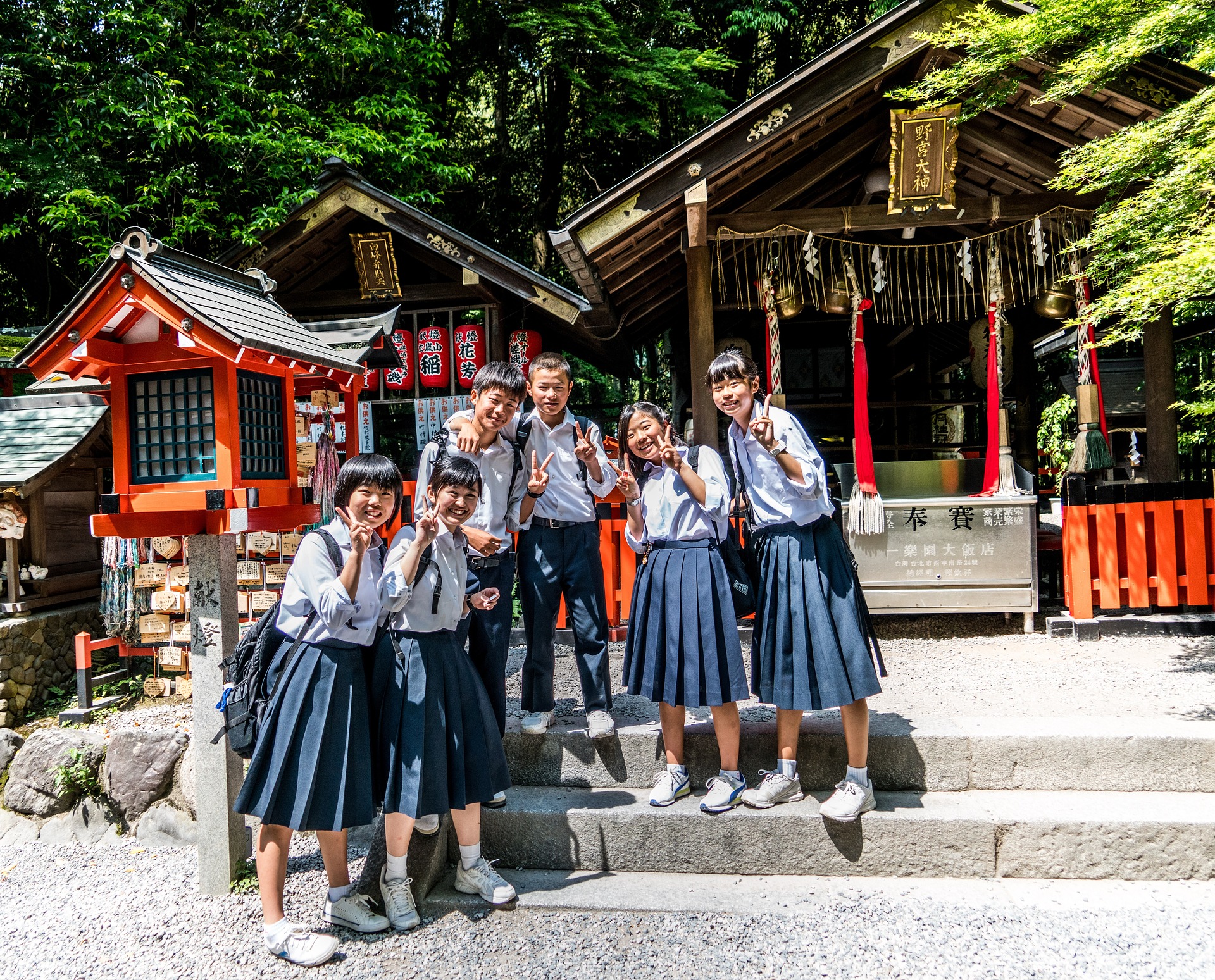 Japanese students in uniforms(white shirt and blue skirt) standing on a stone stair in front of red, Japanese traditional buildings