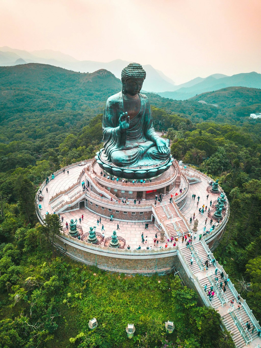 The giant Tian Tan Buddha statue on Lantau Island, Hong Kong, surrounded by green hills and a circular plaza filled with visitors.