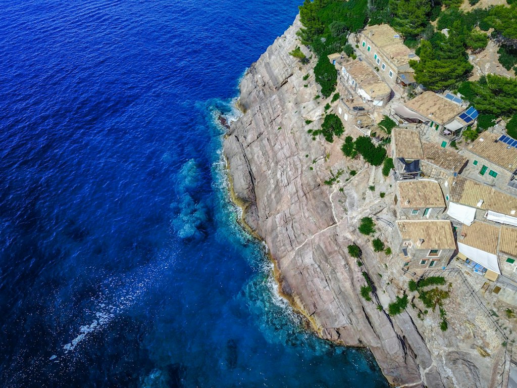 Rocky cliffside with rustic buildings perched above deep blue water, highlighting the contrast between nature and architecture. Fun Facts About Palma de Mallorca 