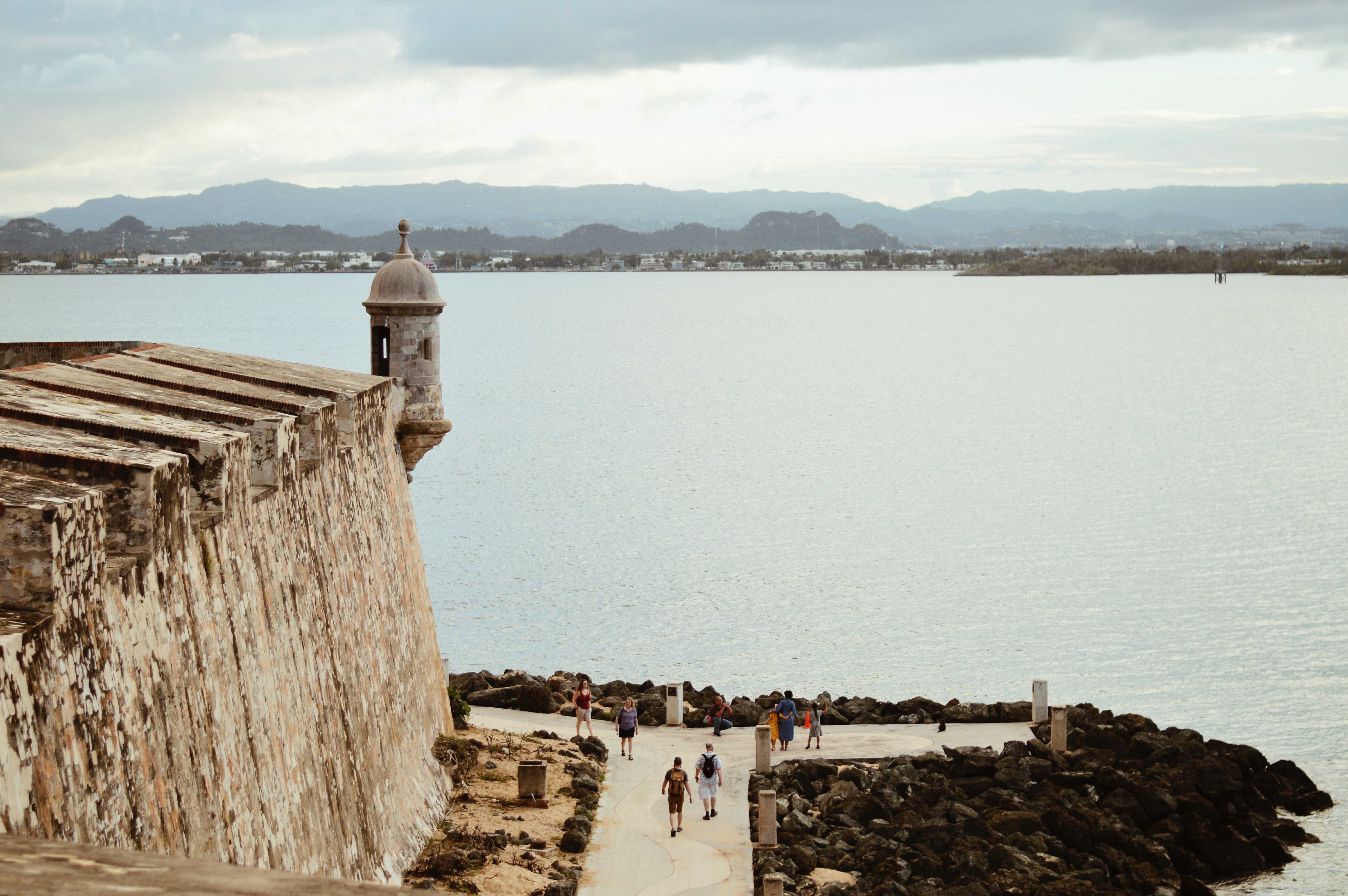 A stone fort sentry tower overlooks the bay as a path leads walkers along the coastline