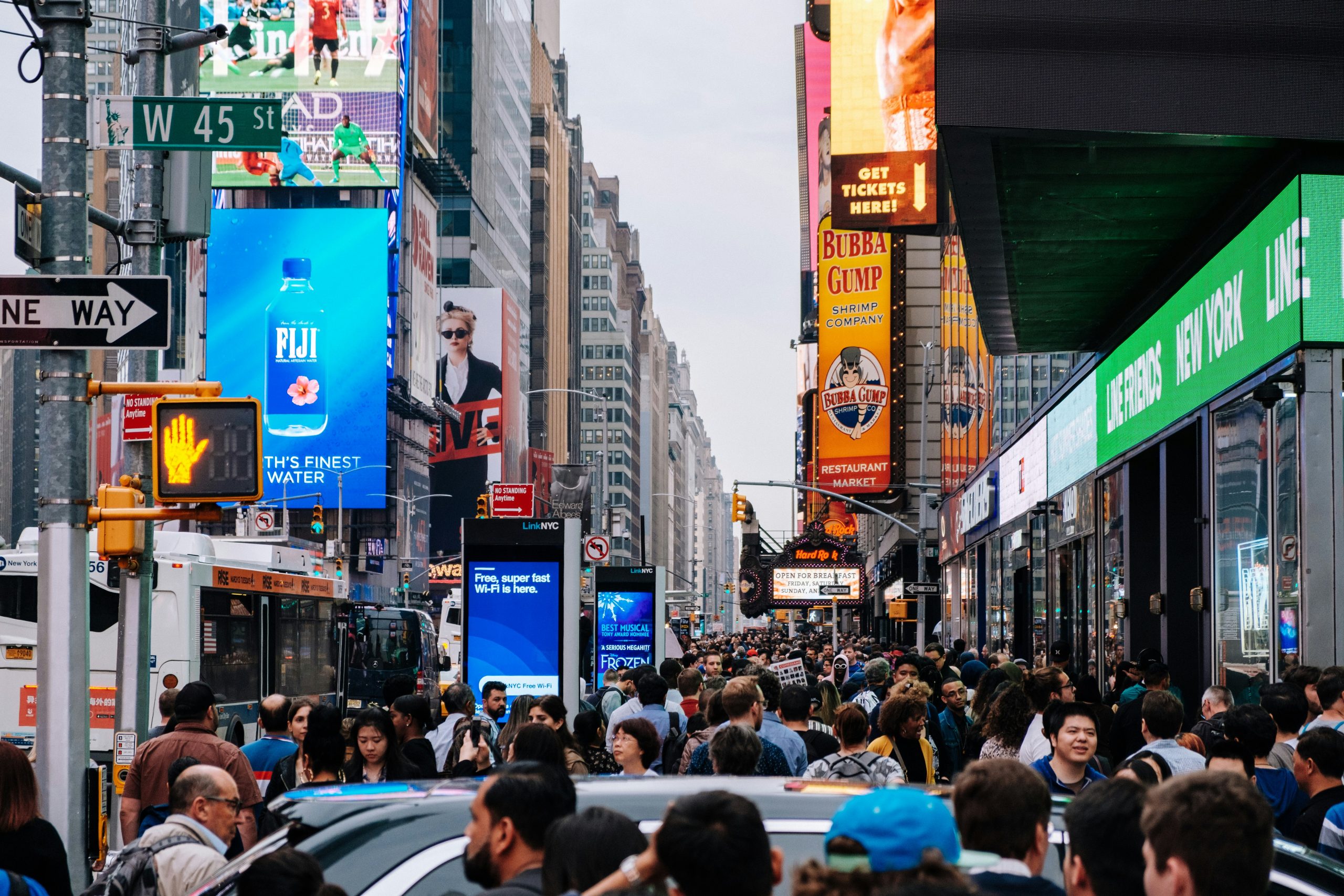Crowded Times Square in New York City with bright digital billboards and bustling crowds.