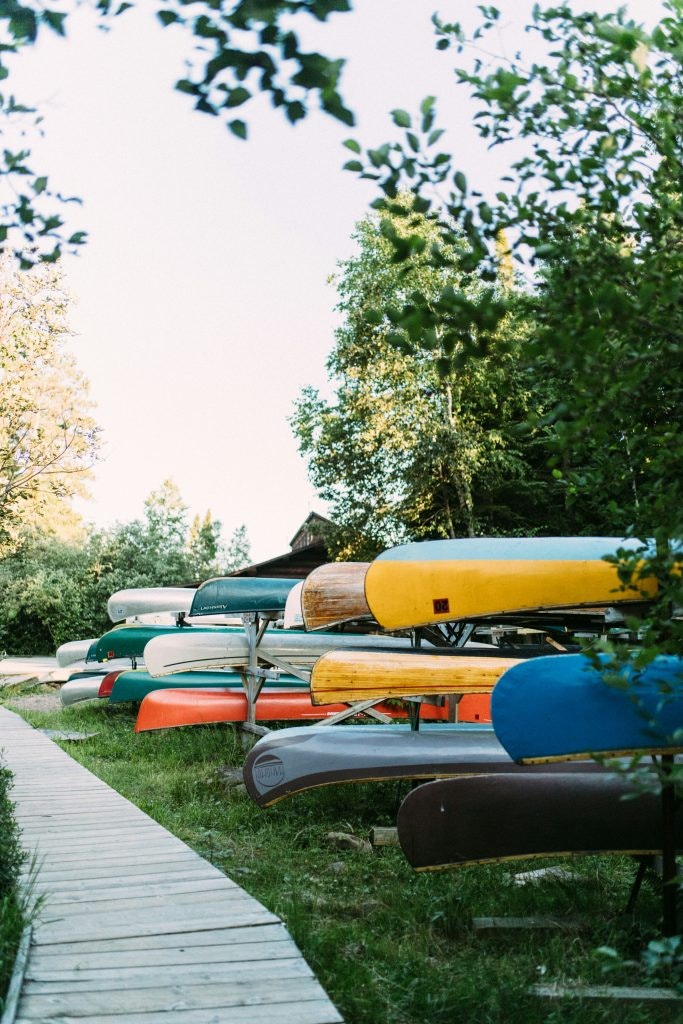 A vibrant array of canoes in various colors is lined up along a wooden trail. Perfect idea for summer volunteer programs for students.