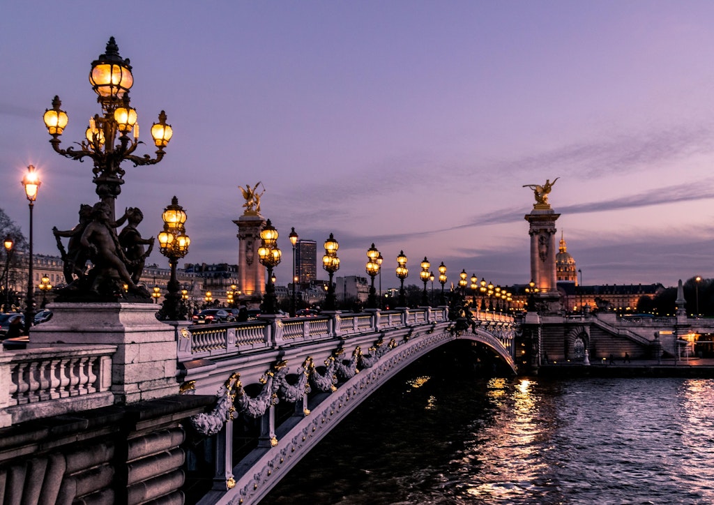 At night, the Paris bridge shines with warm streetlights, highlighting its arches. The light reflects on the water,perfect for evening walks.