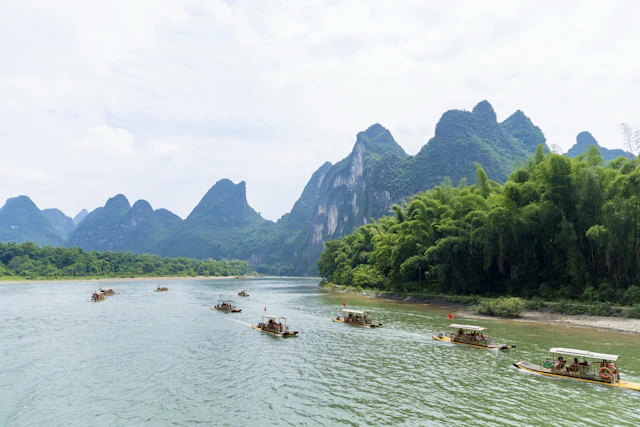 Bamboo rafts pass tree-covered limestone peaks beside the Li River in China