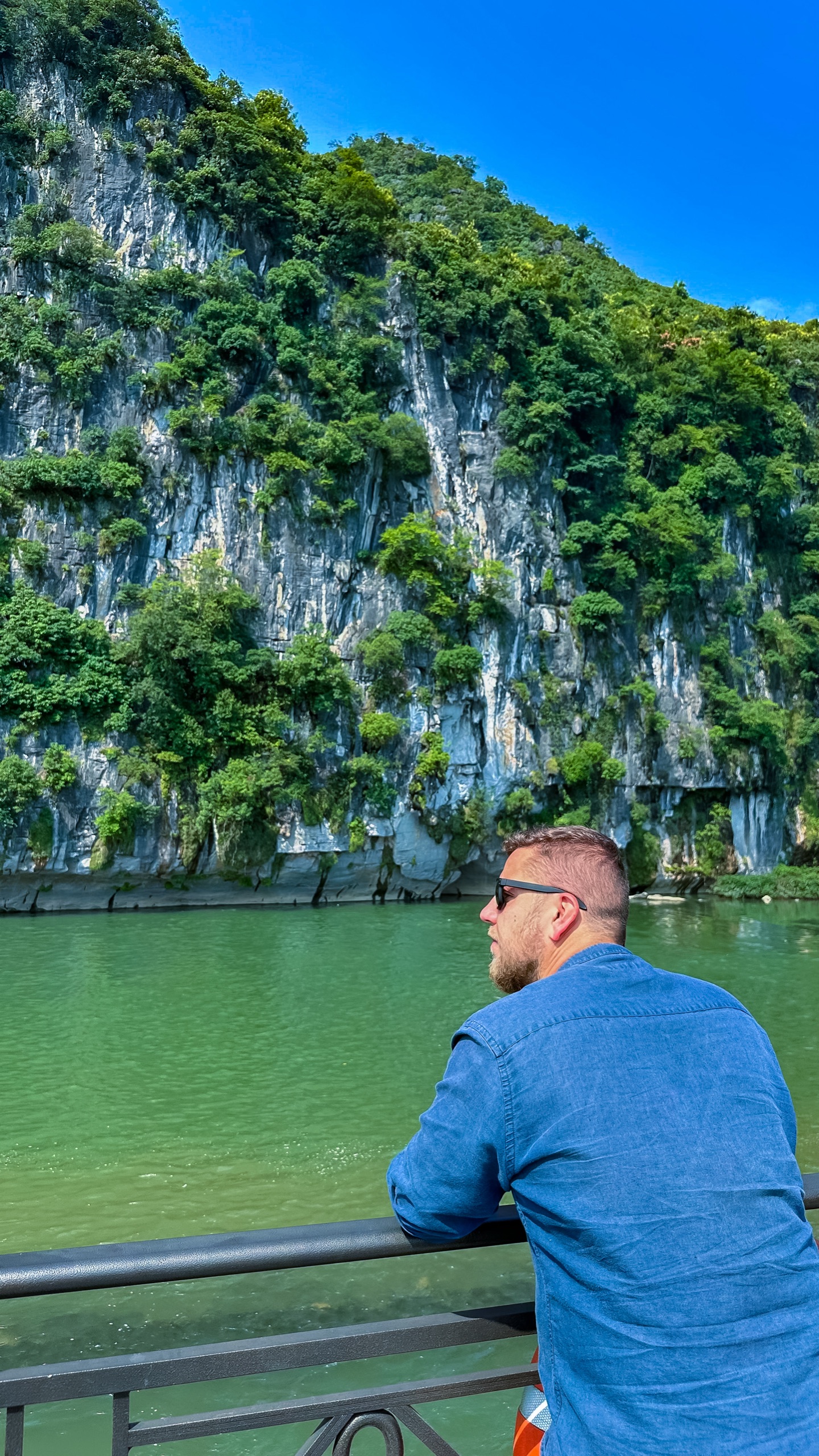 A traveller at the rail of a Li River cruise boat looking up at the limestone karst cliffs near Guilin, China