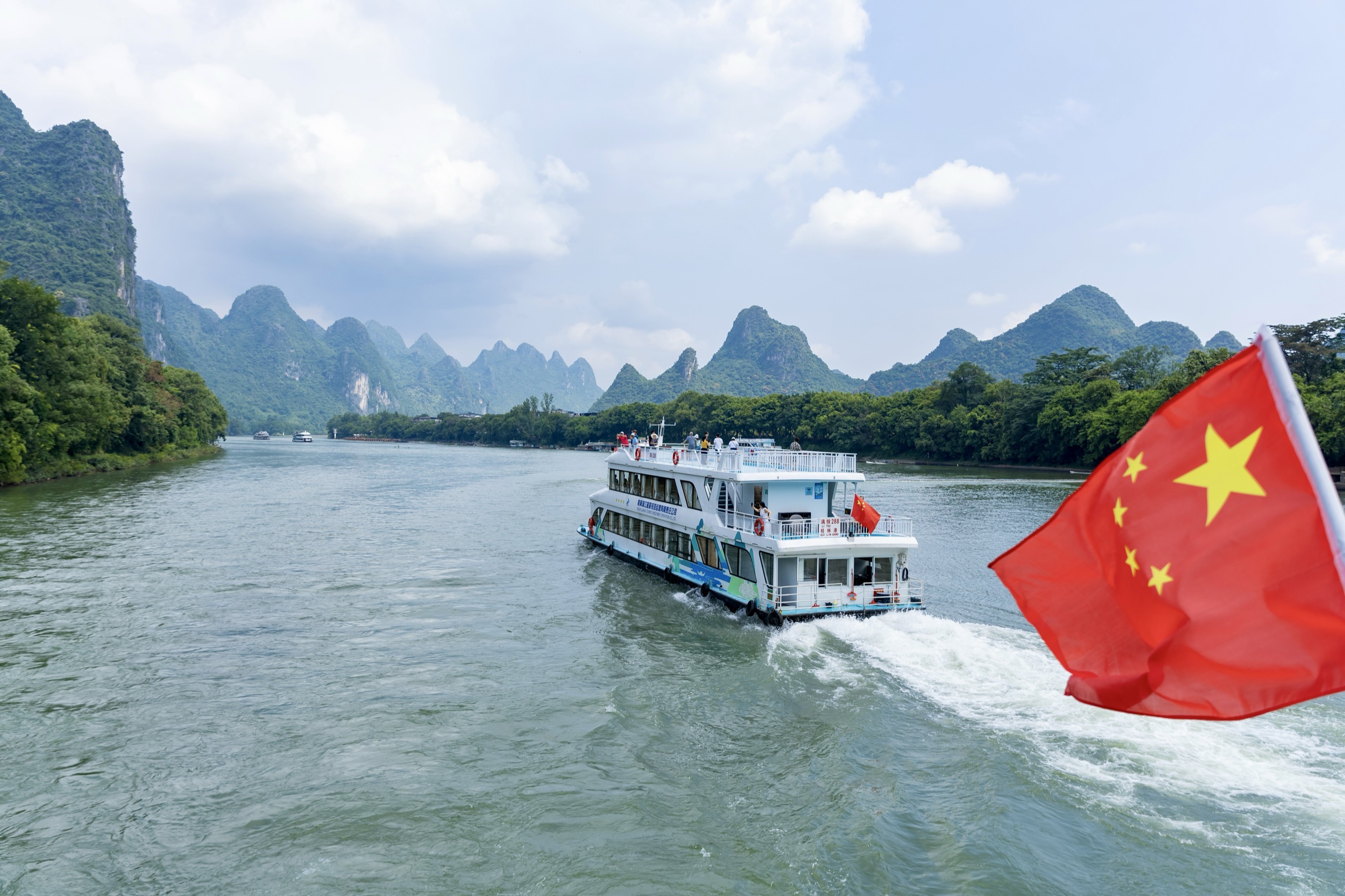 A cruise boat on the Li River between the limestone karst peaks of Guilin, China, flying a Chinese flag