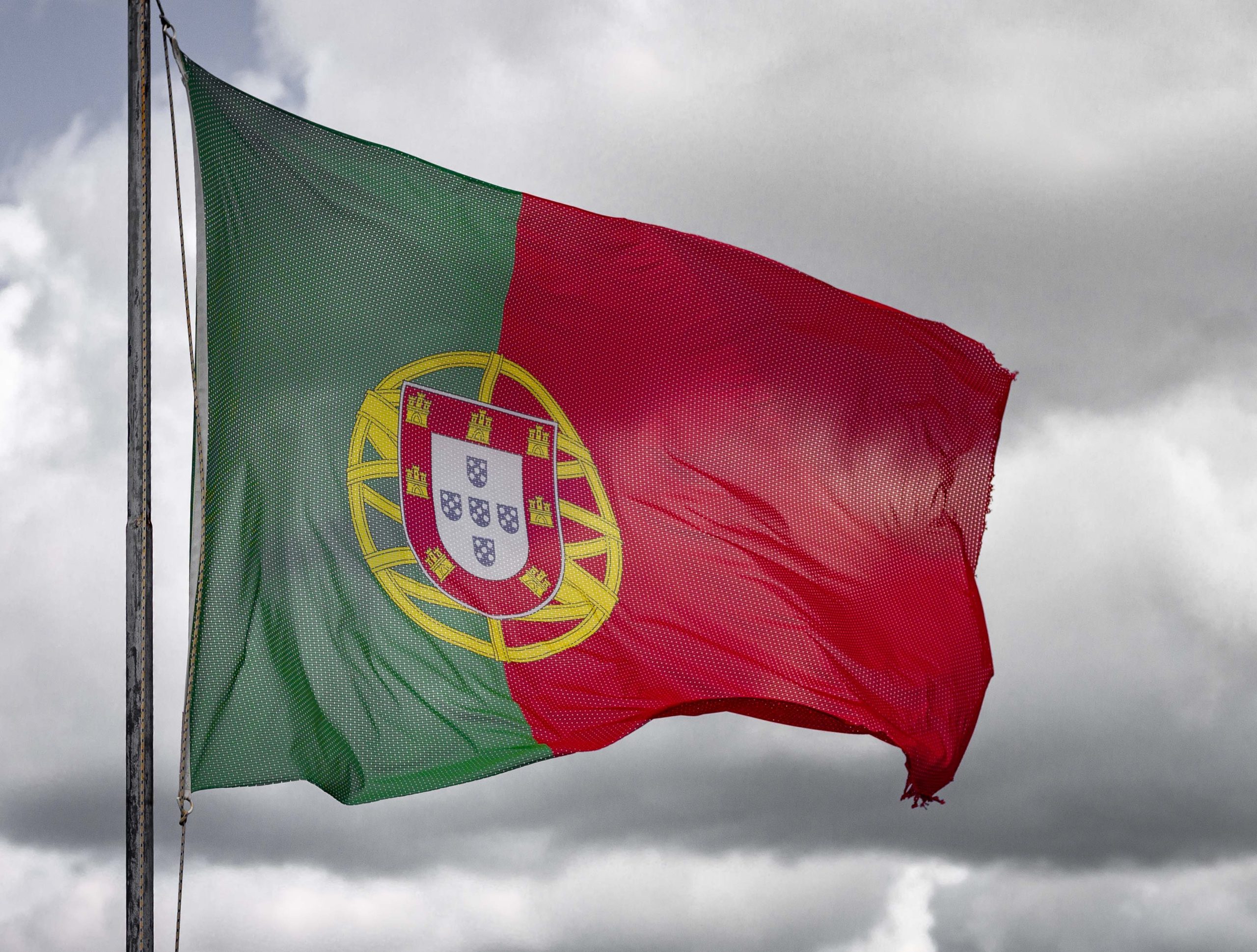 Portugal's flag with its coat of arms ripples against a cloudy sky