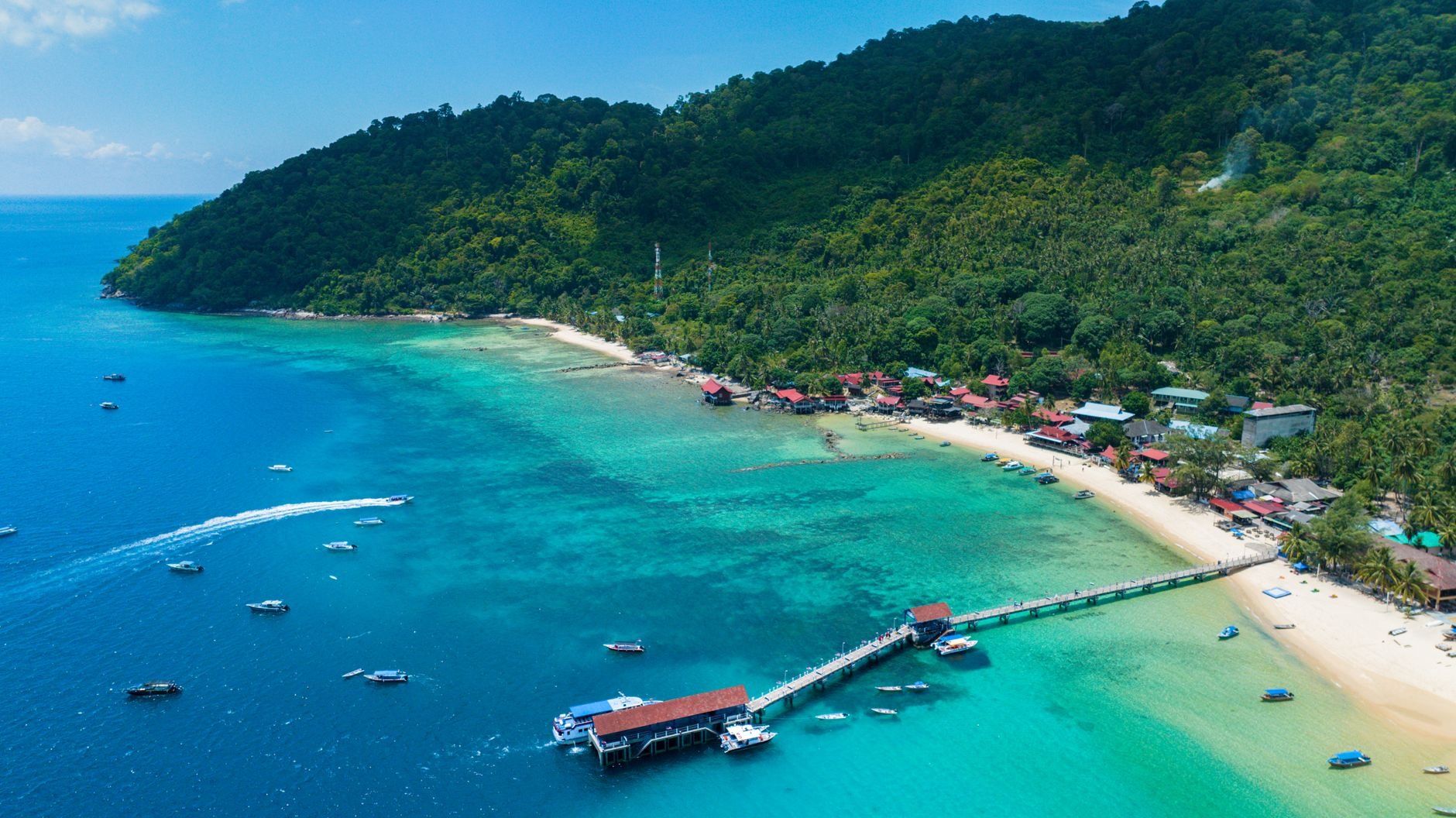 An aerial view of a forested island beach ringed by clear turquoise water.